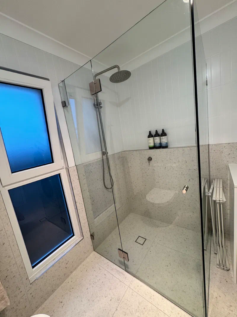Glass-screened shower with a rain shower head and hand shower, stone-look tiled walls and a fold-down shower seat.
