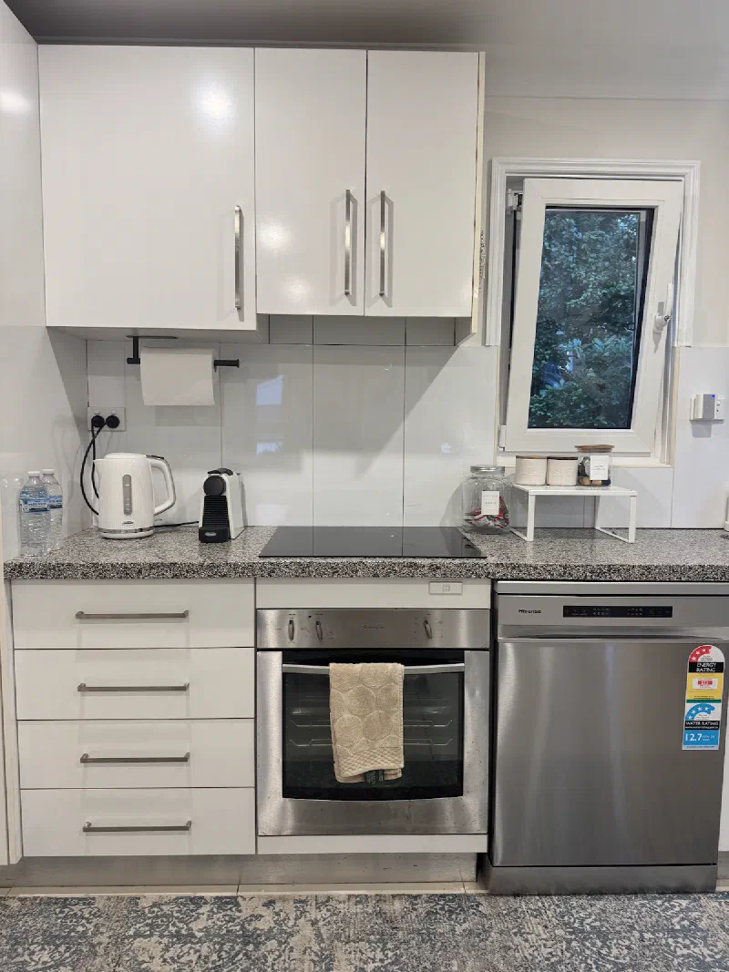 Kitchen bench with a kettle and coffee maker above a black cooktop, with a stainless steel oven and dishwasher below.