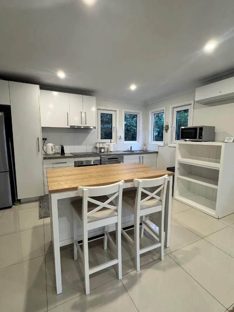 Kitchen with a timber-topped island bench and two white stools, white cabinets, a stainless steel fridge and open shelving.