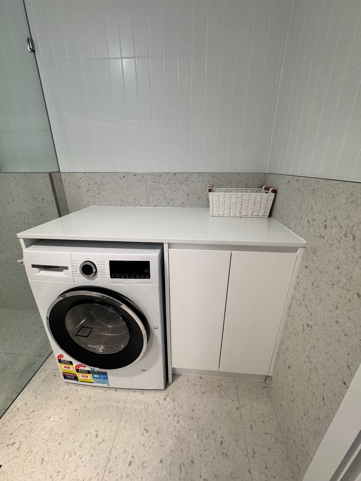 Front-loading washing machine beside a white cupboard in the tiled laundry