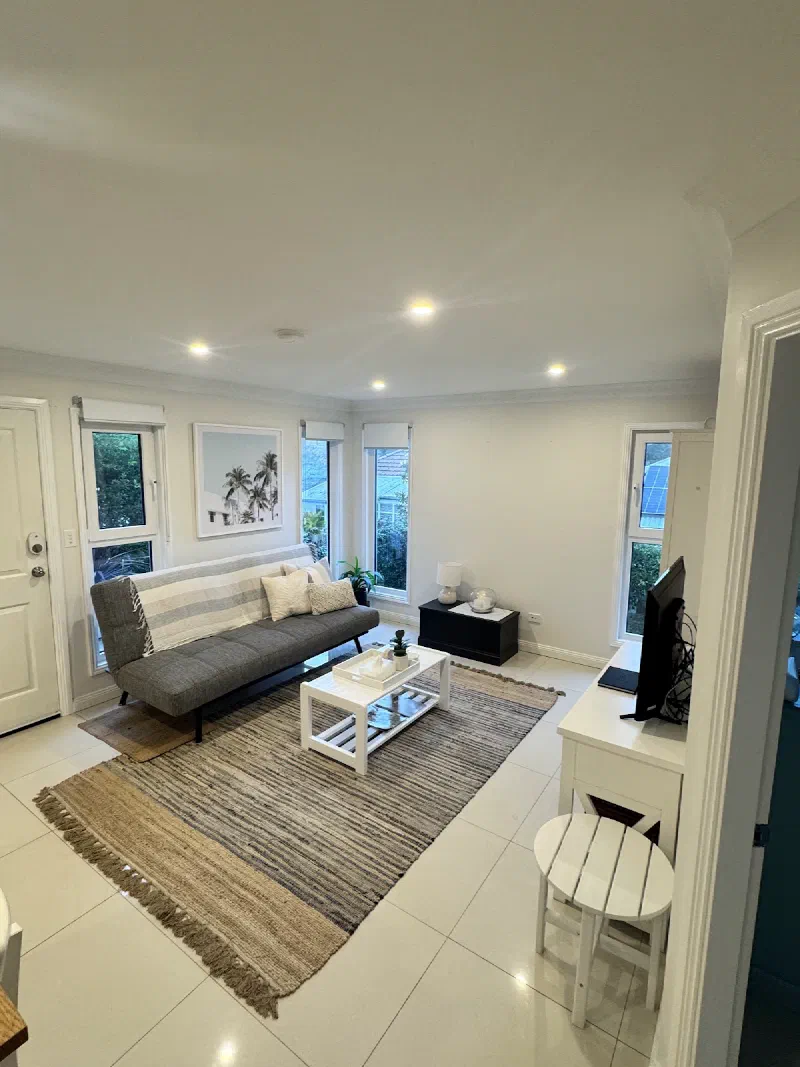 The living area seen from the doorway, with a grey sofa, armchair, coffee table and striped rug beneath downlights.